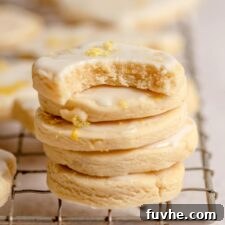A stack of small, round lemon shortbread cookies with icing on a cooling rack. The cookie on top has a bite out of it.