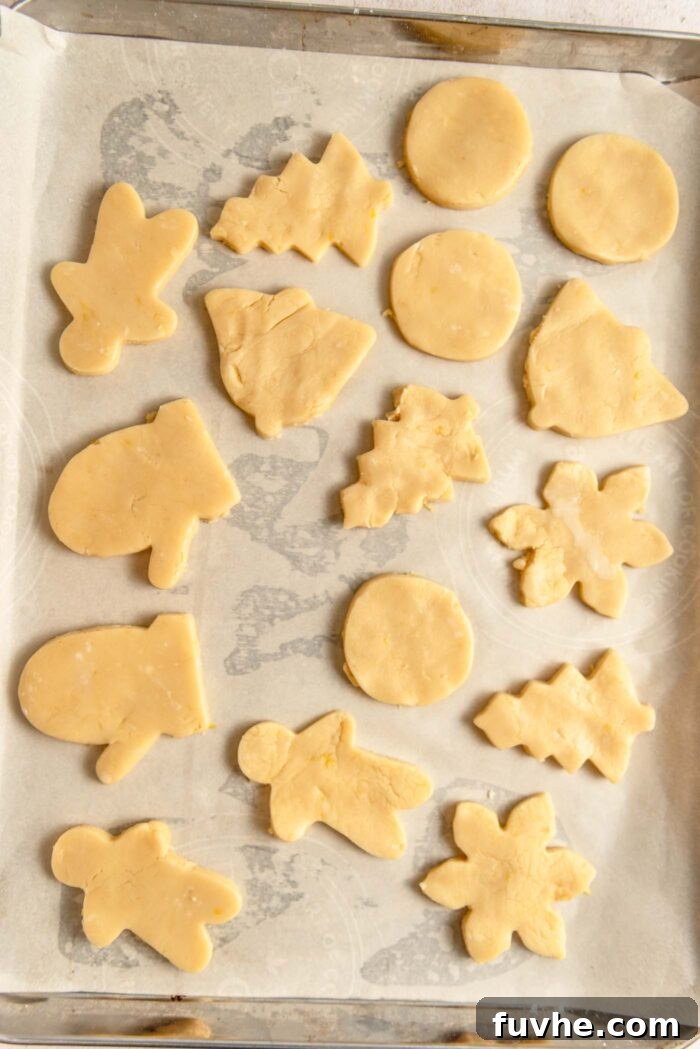 Zesty Lemon Shortbread Bites 7 Raw Christmas-theme shaped shortbread cookies on a baking tray lined with parchment paper.
