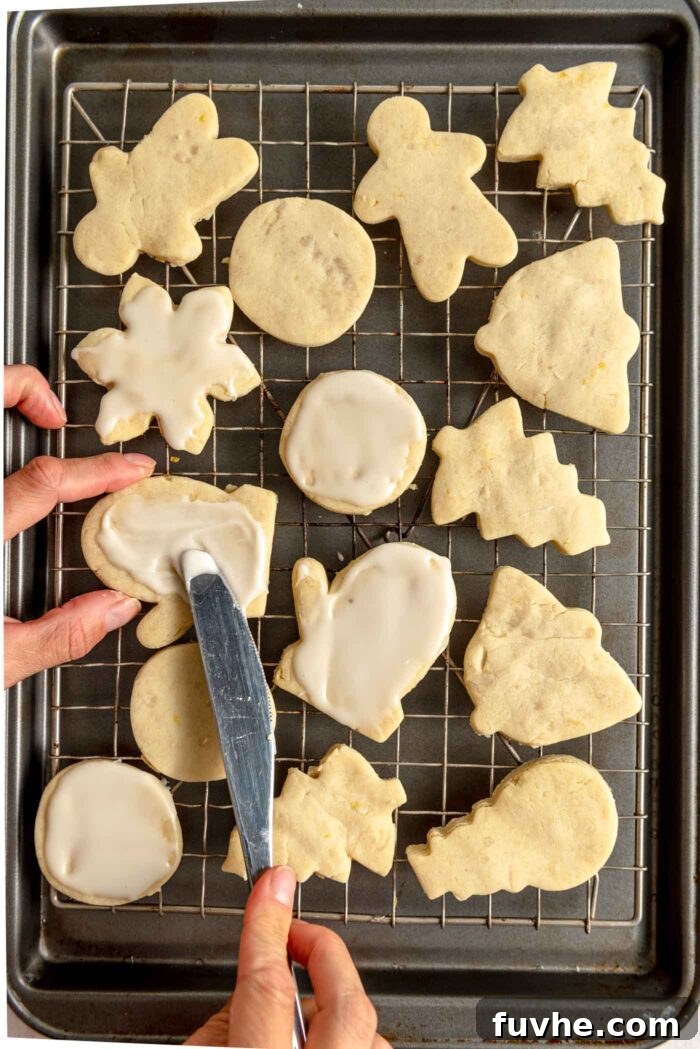 Zesty Lemon Shortbread Bites 9 A hand using a knife to spread icing on a lemon shortbread cookie on a cooling rack.