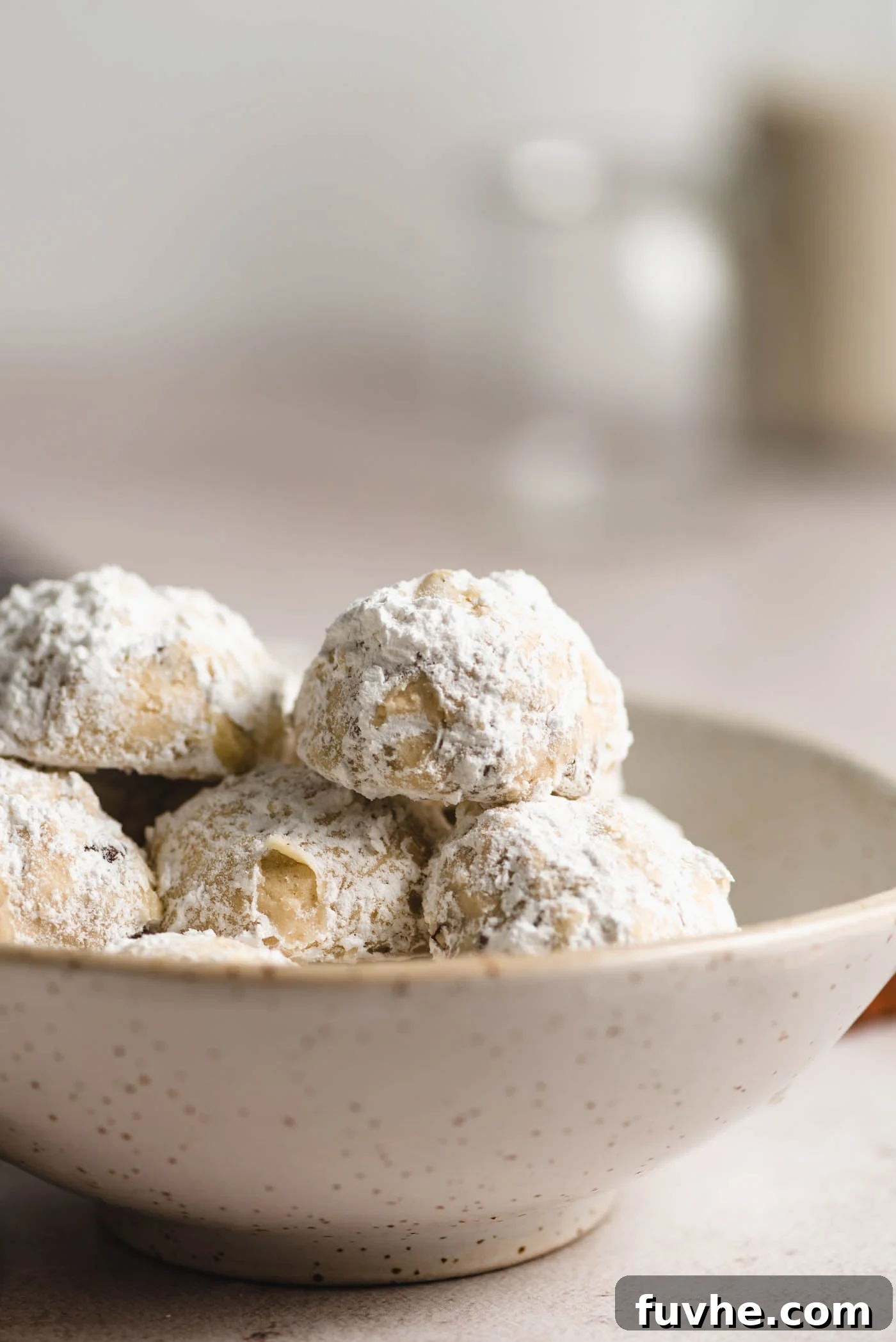 Melt-in-Your-Mouth Vegan Pecan Snowballs 2 Powdered sugar-coated snowballs cookies in a small bowl.