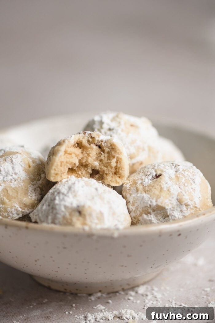 Melt-in-Your-Mouth Vegan Pecan Snowballs 11 Pecan snowball cookies in a small bowl. The cookie on top has a bite out of it so you can see the inside texture.