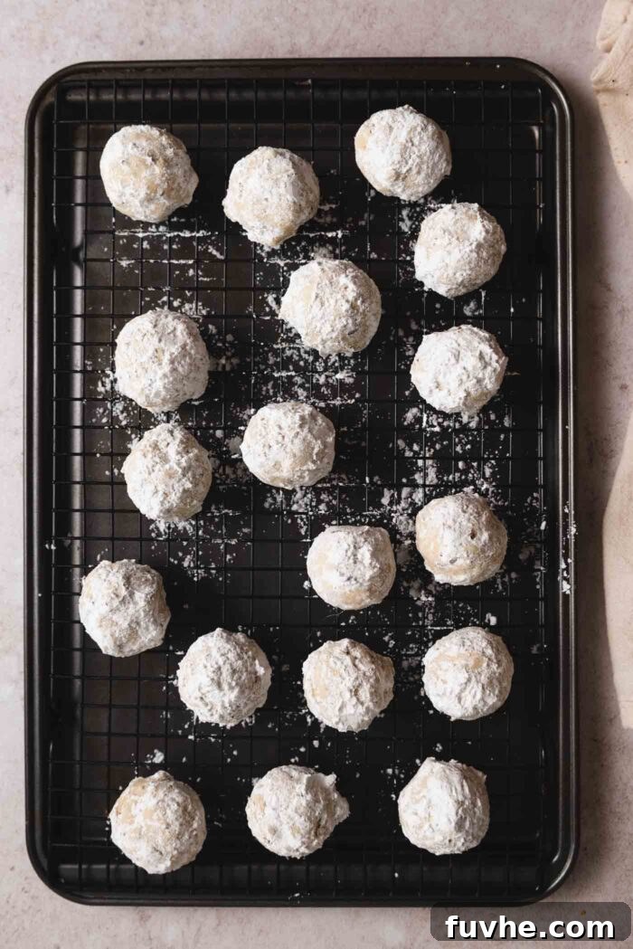 Melt-in-Your-Mouth Vegan Pecan Snowballs 9 18 pecan snowball cookies on a baking cooling rack sitting on top of a baking sheet.