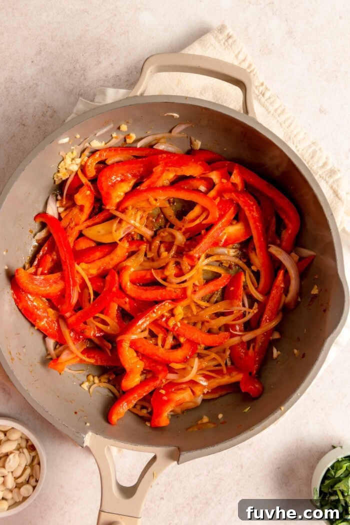 Sliced red bell peppers, red curry paste, shallot, and ginger cooking in a non-stick pan.
