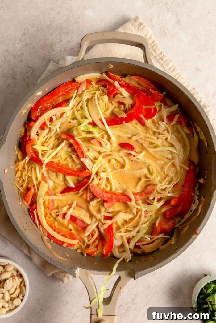 Cabbage and red bell pepper simmering in a vibrant red curry sauce in a pan.