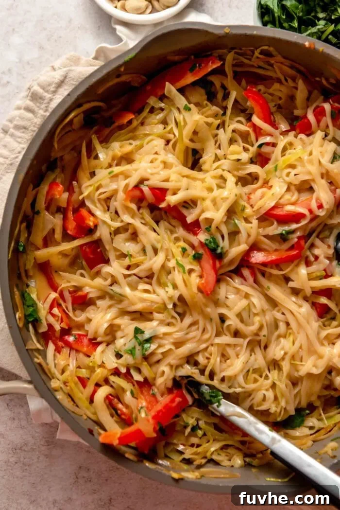 Overhead view of a large pan of Thai red curry noodles with cabbage and red pepper, coated in sauce.