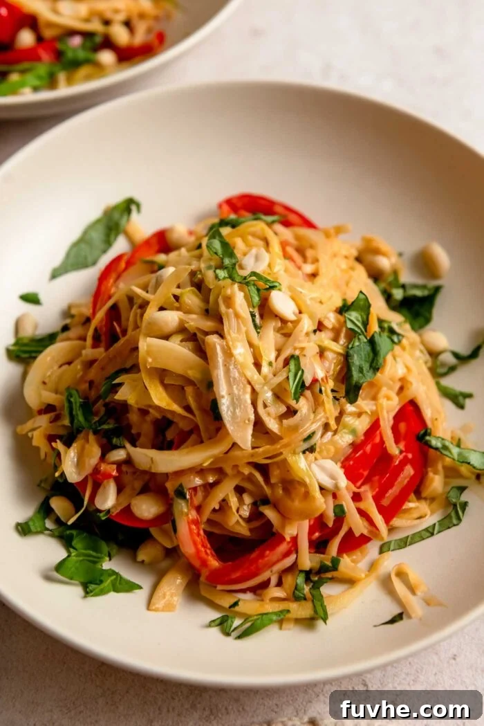 A beautifully plated bowl of Thai red curry noodles, topped with fresh basil and roasted peanuts.