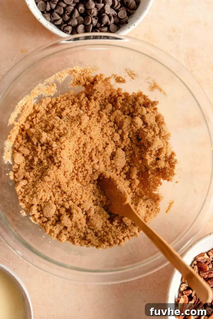 Graham cracker crumbs mixed with melted vegan butter in a bowl, with a small wooden spoon resting in it, ready to be pressed into the crust.
