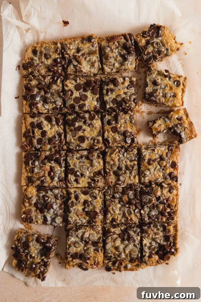 An overhead view of a pan of baked vegan 7 layer cookies bars, perfectly cut into 24 squares. A few squares are pulled aside, revealing the thick, gooey layers of coconut, chocolate chips, and pecans on a graham cracker crust.