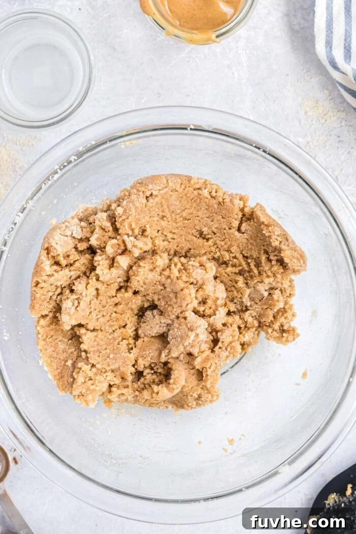 Spoonable Peanut Butter Cookie Dough 5 Smooth, rich edible peanut butter cookie dough sits perfectly blended in a clear glass mixing bowl, ready for shaping.