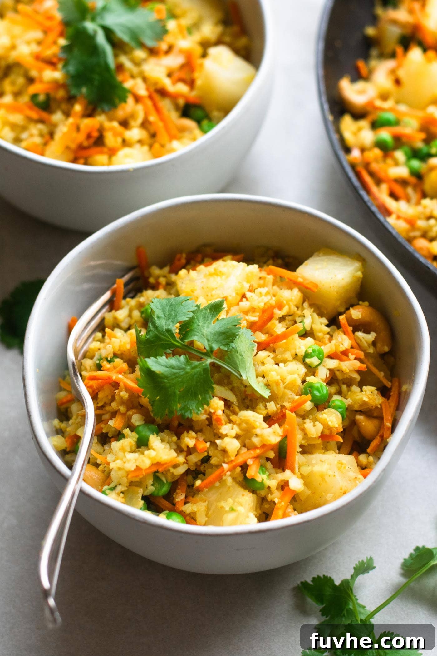 A vibrant skillet filled with Vegan Pineapple Cashew Cauliflower Rice, showcasing golden cauliflower, bright pineapple chunks, green peas, and crunchy cashews, ready to be served with a wooden spoon.