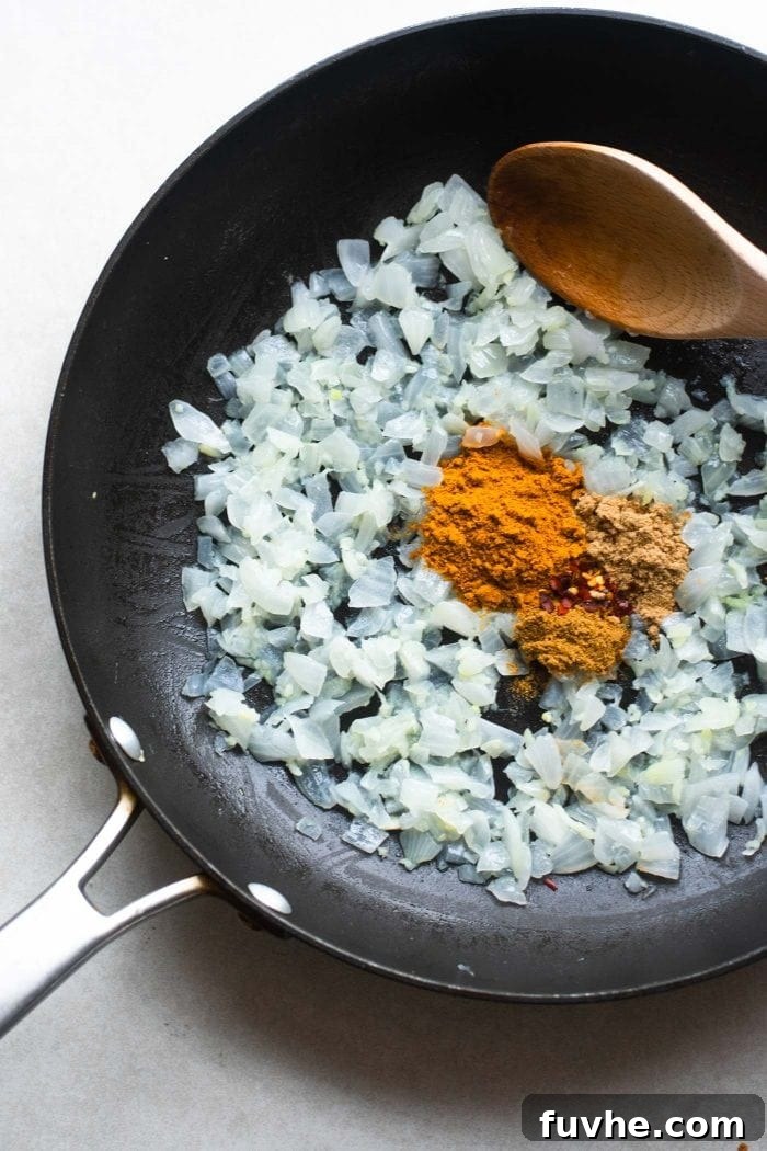 Sautéed onions and garlic coated with a rich blend of curry powder, cumin, coriander, and red pepper flakes, sizzling gently in a skillet, filling the air with enticing aromas.