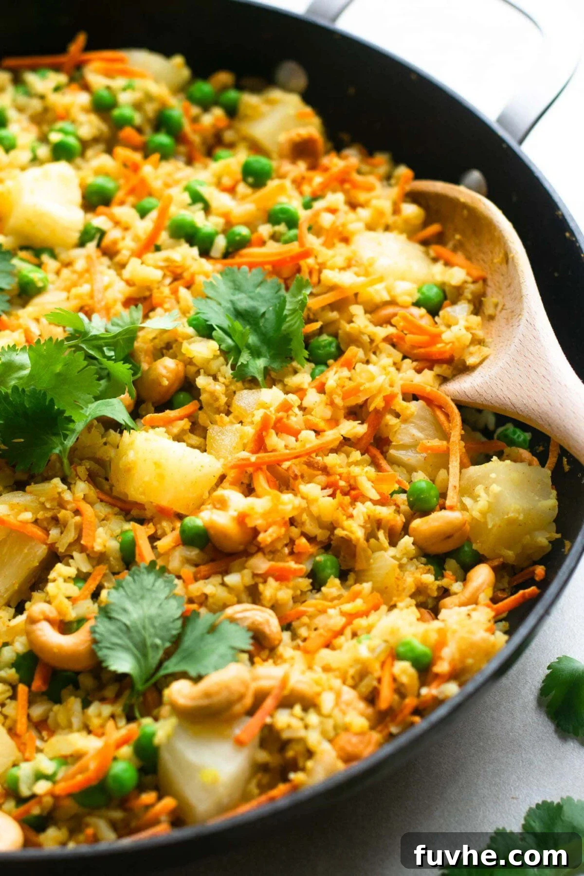 The completed Vegan Pineapple Cashew Cauliflower Rice in a large skillet, showcasing a colorful blend of riced cauliflower, golden pineapple, green peas, and toasted cashews, ready to be seasoned and served.