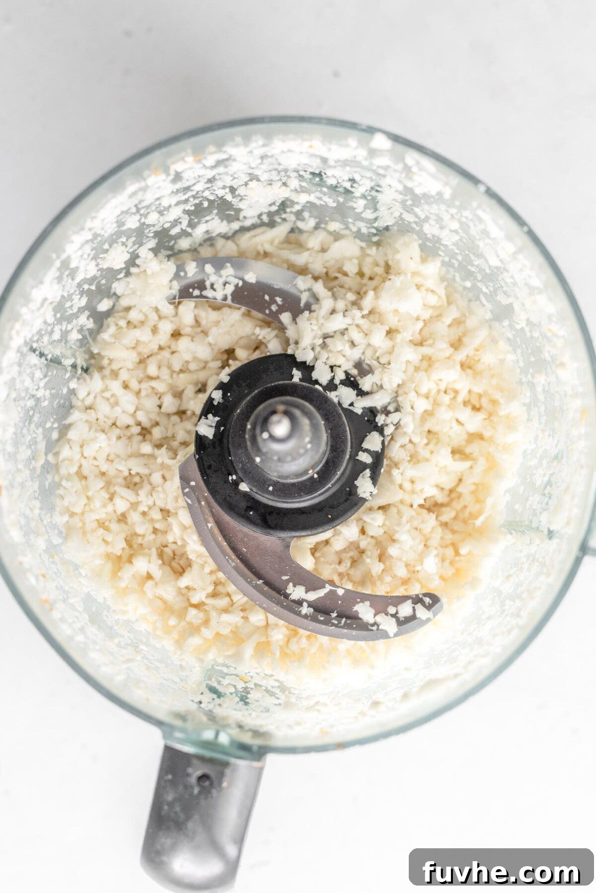 Fresh cauliflower florets being pulsed into rice-like granules in a food processor, demonstrating the easy homemade method for creating cauliflower rice.