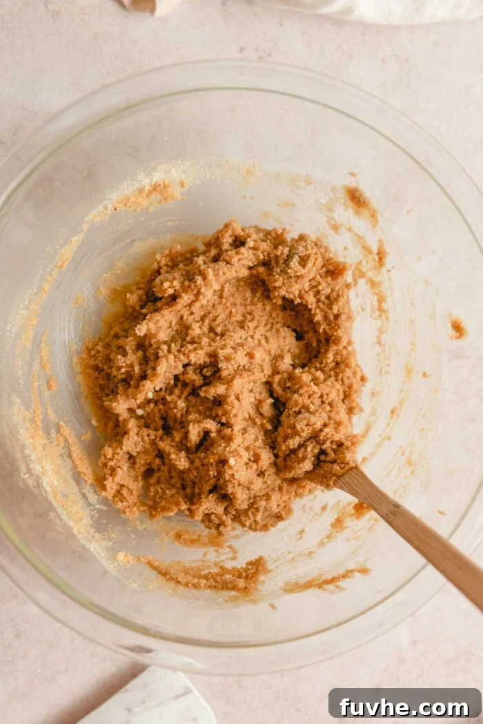 Almond flour peanut butter cookie dough in a glass mixing bowl with a wooden spoon.
