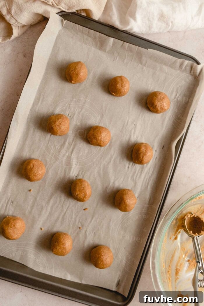 12 balls of of peanut butter cookie dough on a baking sheet lined with parchment paper.