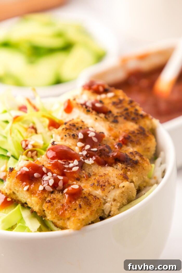 Close up of beautifully golden-fried tofu katsu slices arranged appealingly in a bowl with fresh shredded cabbage and crisp cucumber, ready to be enjoyed.