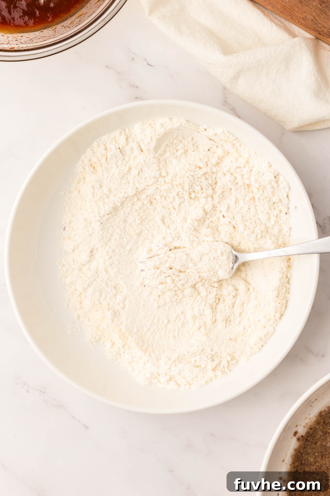 Two shallow bowls, one containing all-purpose flour seasoned with spices, and the other filled with crispy panko breadcrumbs, forming part of the breading station.