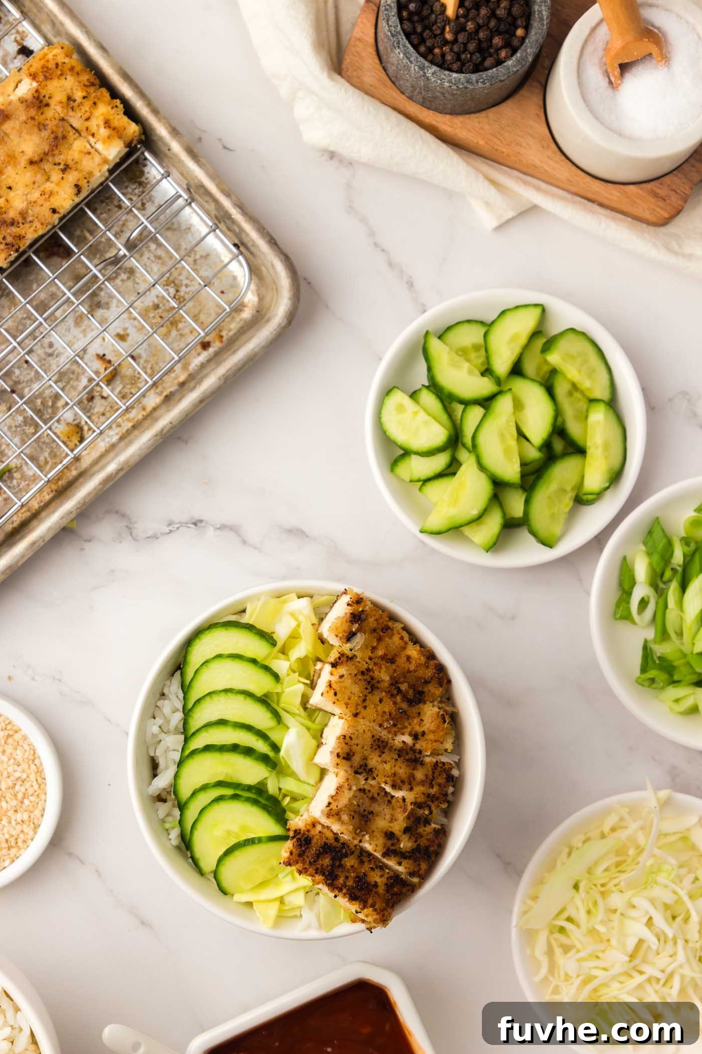 A close-up shot of a beautifully assembled vegan tofu katsu rice bowl, featuring perfectly sliced crispy tofu, fresh cabbage, and cucumber, drizzled with sauce.