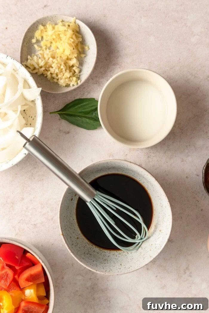 Stir fry sauce mixed together in a small bowl with a whisk beside a small bowl of cornstarch slurry and another bowl of minced garlic and ginger.