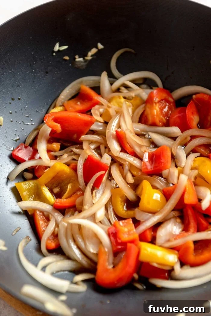 Stir fried peppers and onions in stir fry sauce cooking in a large wok.