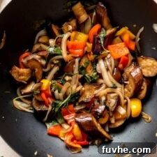 Stir fried Thai basil eggplant cooking in a wok with bell peppers and onions.