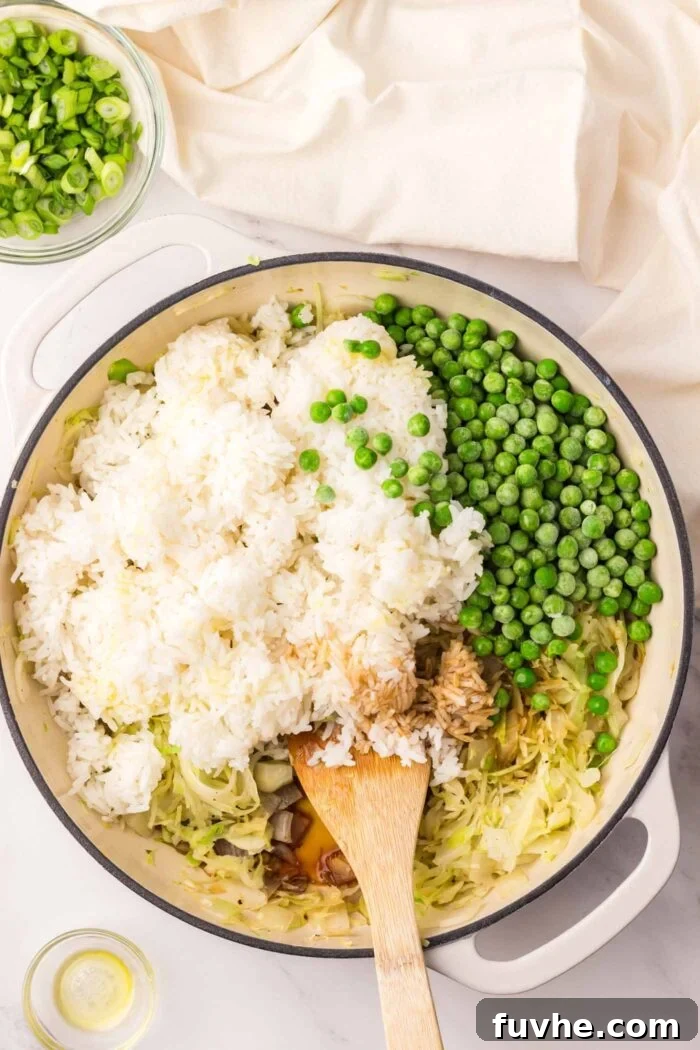 The rice, green peas, and cabbage mixture sizzling in a large skillet, absorbing the aromatic sauces.
