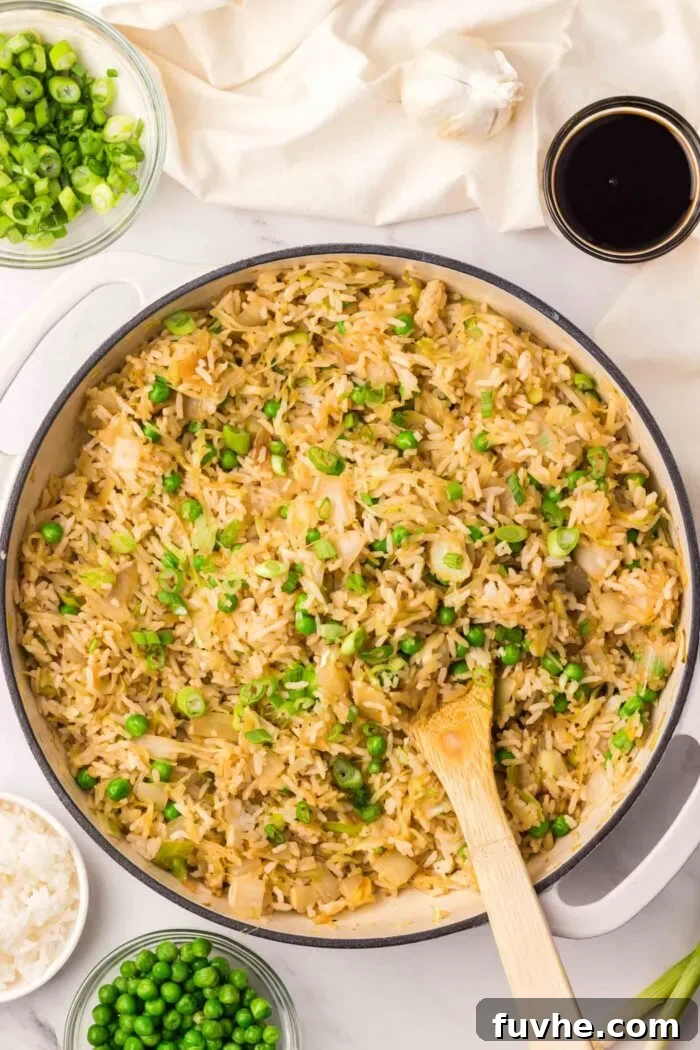 A large skillet brimming with colorful cabbage fried rice, featuring visible green peas and scallions, freshly cooked and ready to serve.
