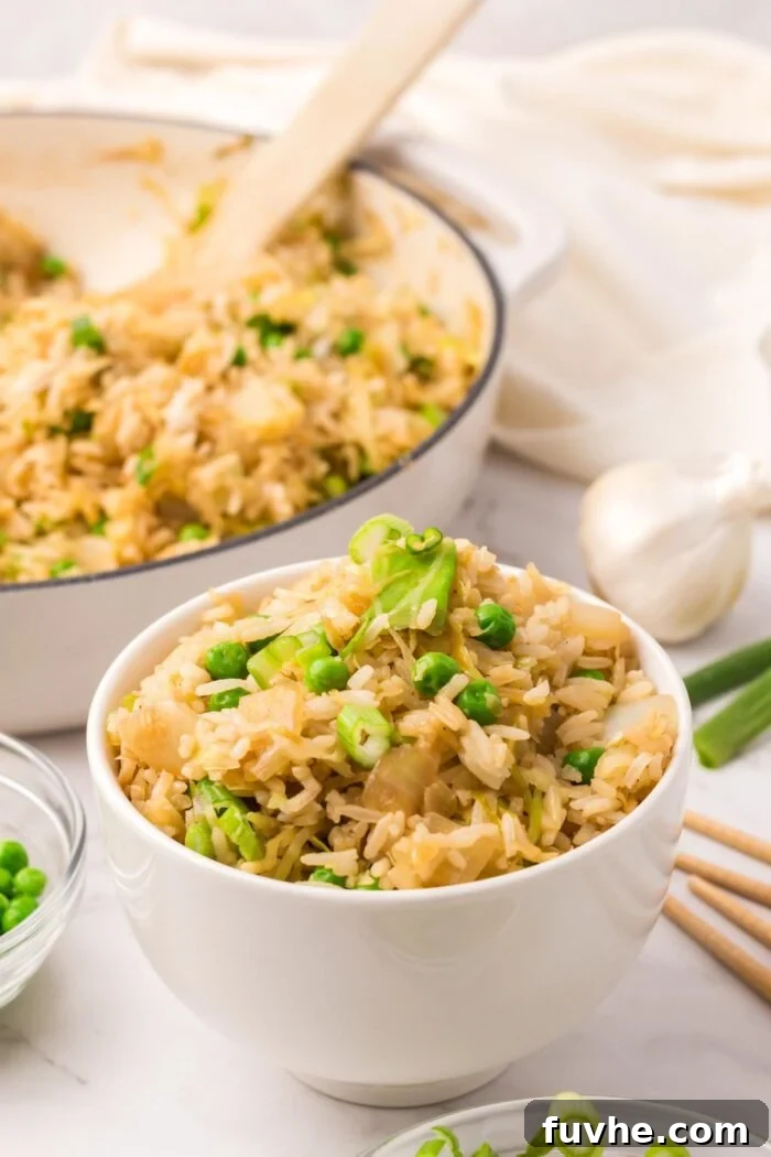A beautiful presentation of cabbage fried rice: a serving bowl alongside a large skillet filled with the fresh dish, featuring a wooden spatula.