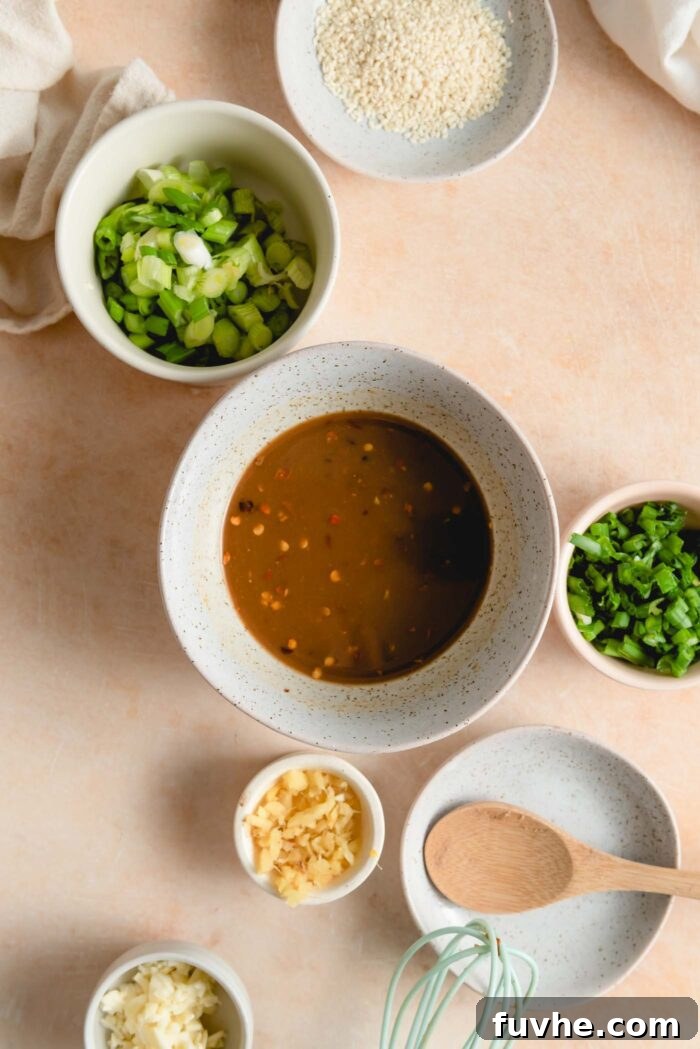 A soy-based sauce with chili flakes in it in a small bowl with smaller bowls of minced garlic, ginger and green onion beside it, ready for cooking.