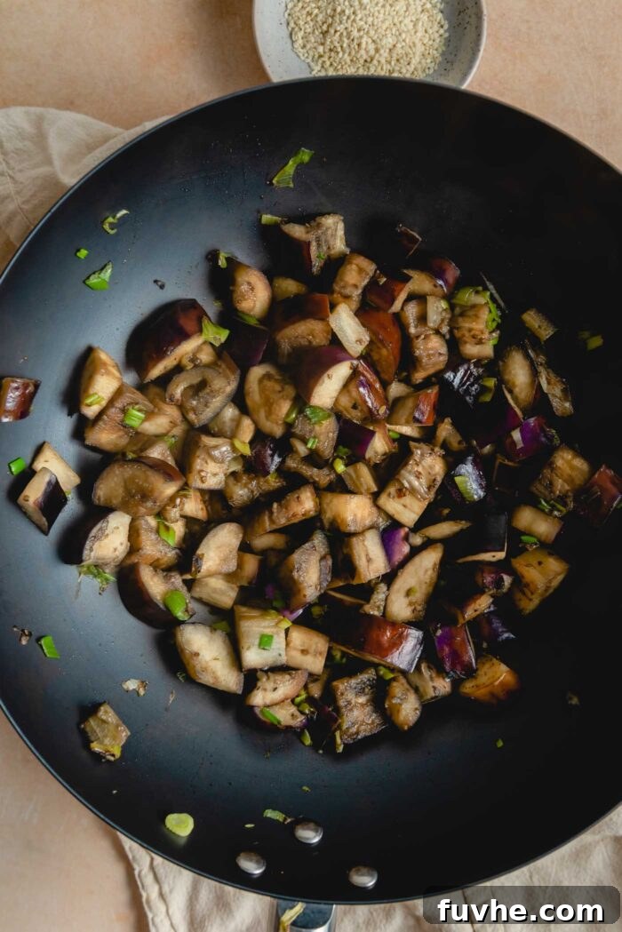 Stir fried cooked eggplant and green onion in a large wok, illustrating the golden-brown perfection.