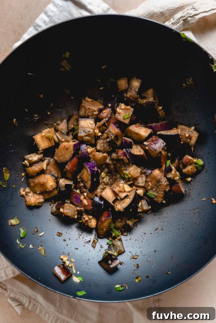 Eggplant stir fry with green onion, garlic and ginger simmering in the miso sauce in a wok.