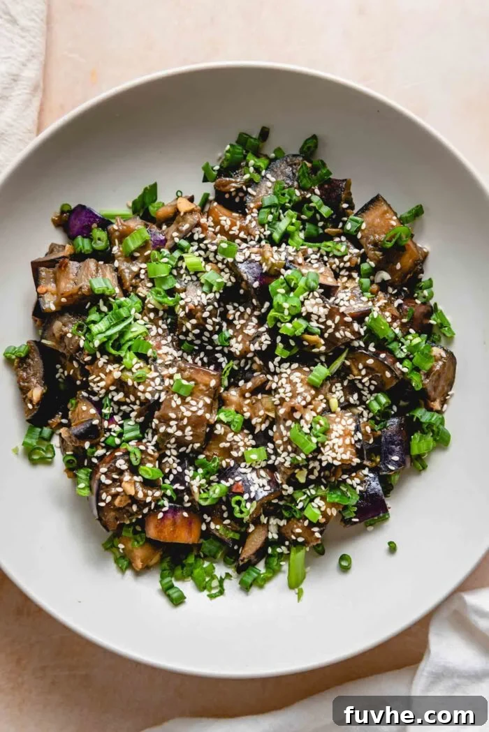 Stir fried eggplant topped with green onions and sesame seeds in a bowl, ready to be enjoyed.