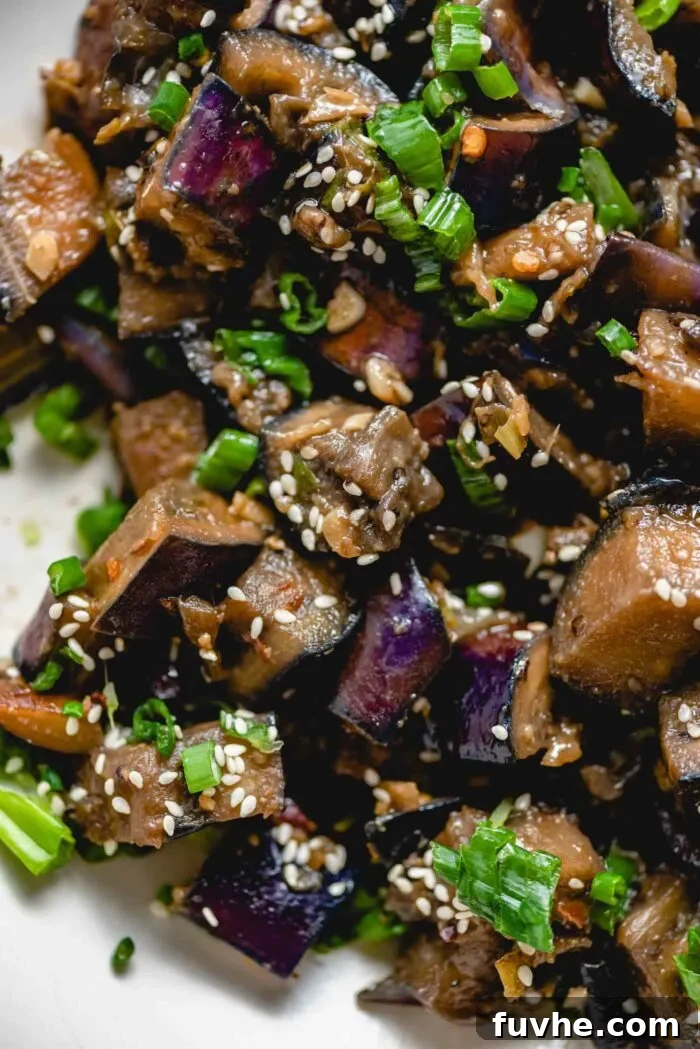 Close up of stir fried eggplant with green onion and sesame seeds in a bowl, highlighting the texture and garnishes.
