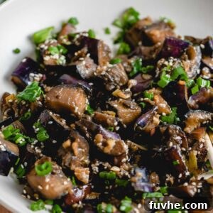 Close up of stir fried eggplant with green onion and sesame seeds in a bowl, ready to be enjoyed.