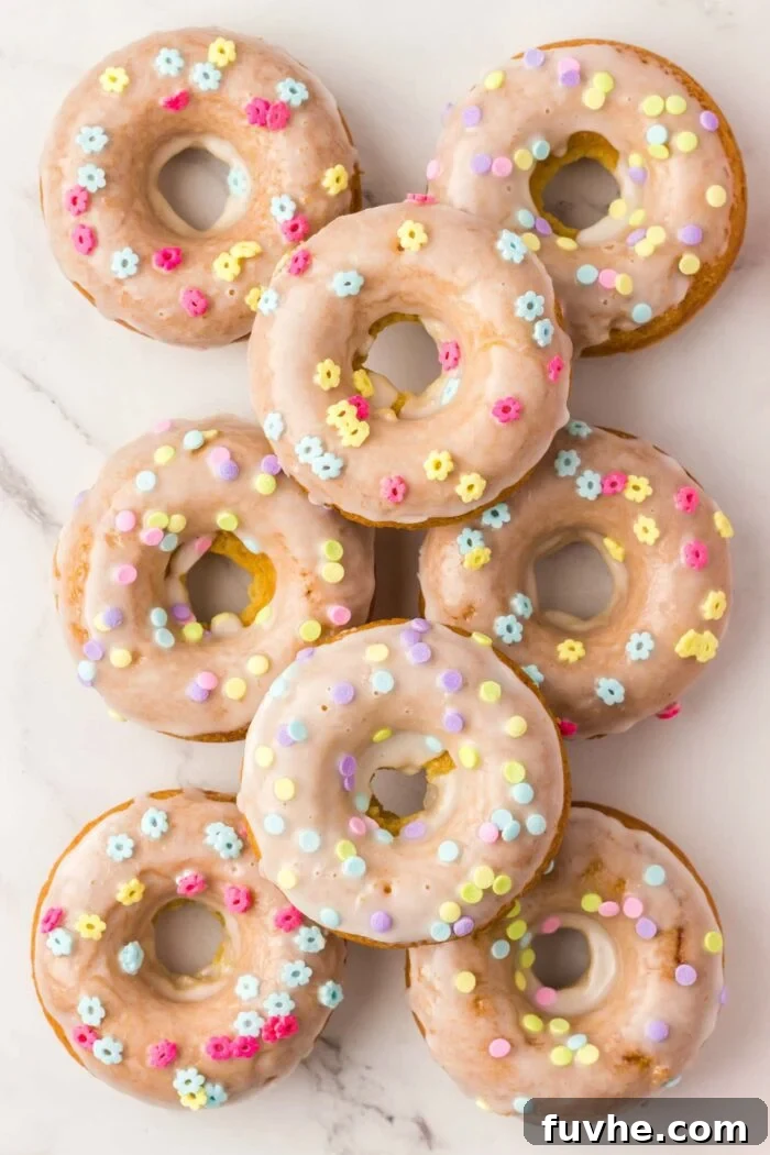 Overhead view of 8 baked and glazed donuts topped with small sprinkles shaped like flowers.