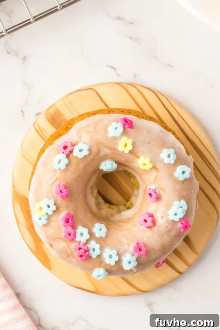 Overhead view of a glazed donut with sprinkles on a small round wooden cutting board.