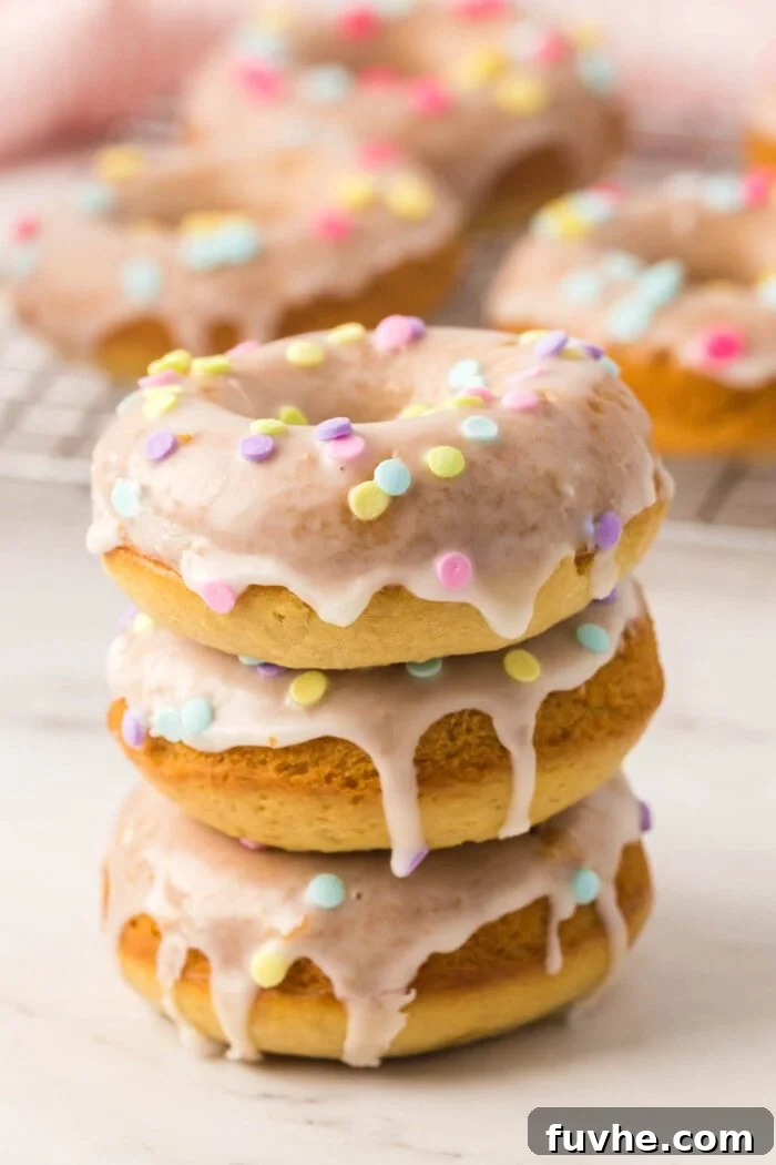 A stack of 3 glazed donuts with sprinkles with more donuts in the background.