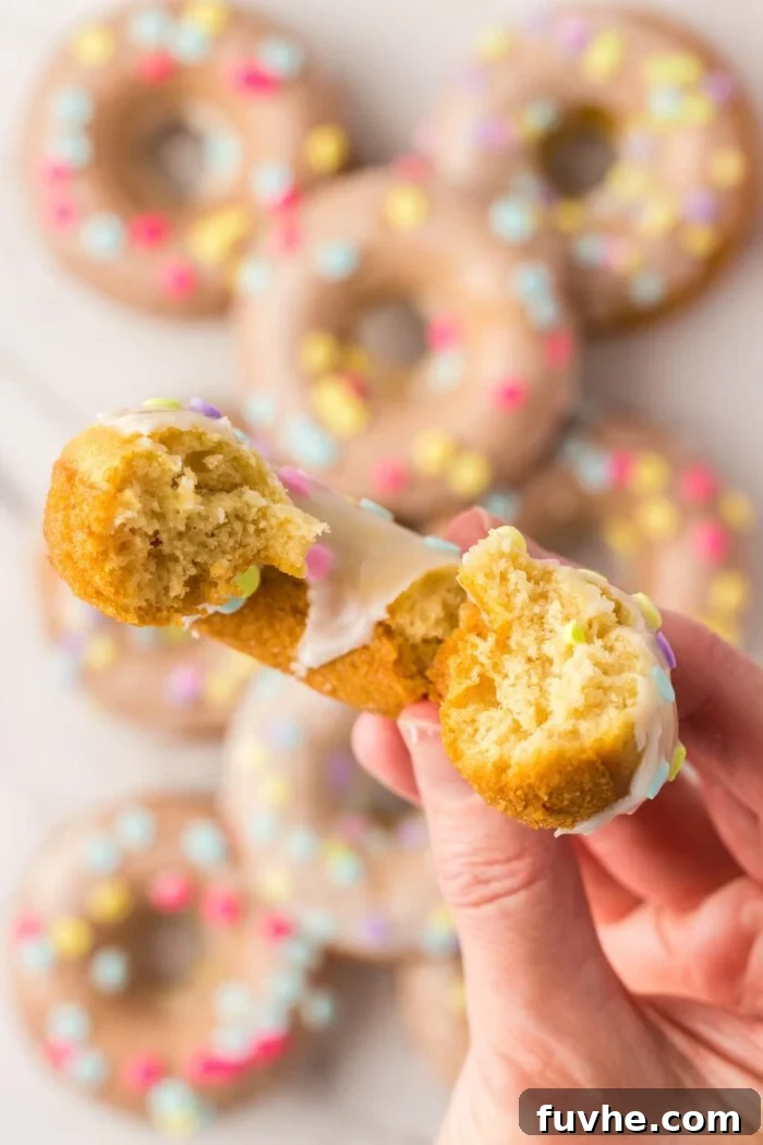 A hand holding a half eaten glazed donut toward the camera so you can see the texture inside.