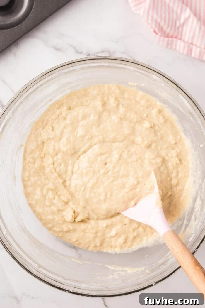 Raw donut batter in a glass mixing bowl with a spatula in it.