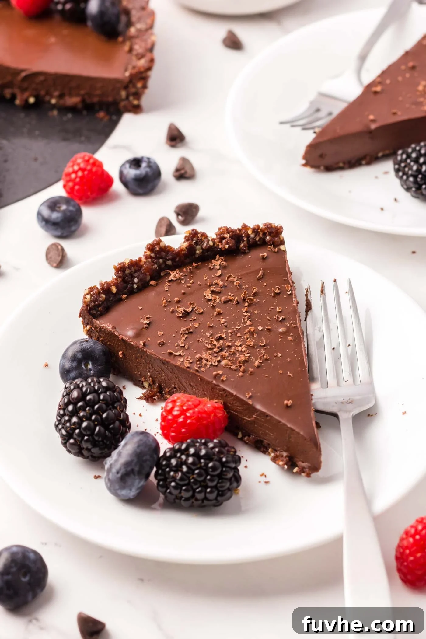 A slice of a chocolate tart with chocolate crust on a small plate with a few raspberries and blackberries on it.