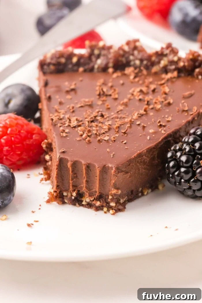 A slice of vegan chocolate tart with a bite out of it on a small plate with a few fresh berries on it.