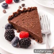 A slice of a chocolate tart with chocolate crust on a small plate with a few raspberries and blackberries on it.