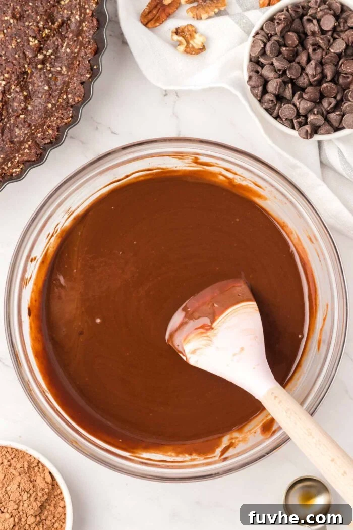 A creamy melted chocolate mixture in a mixing bowl with a spatula in it.