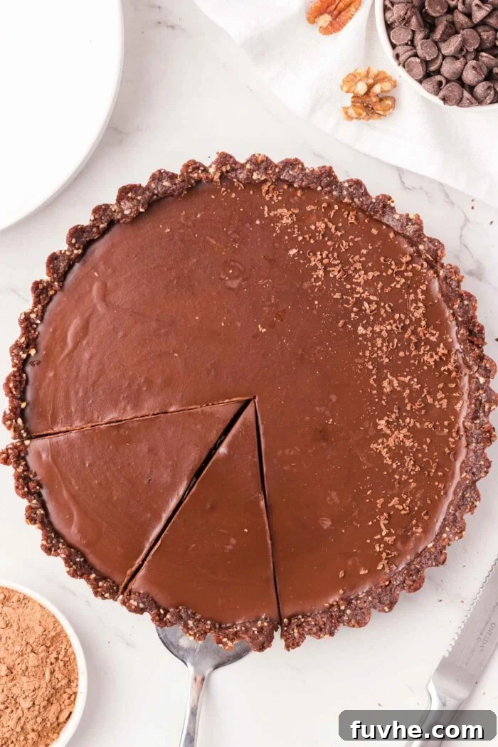 A chocolate ganache tart sprinkled with cocoa powder with two slices cut into it.