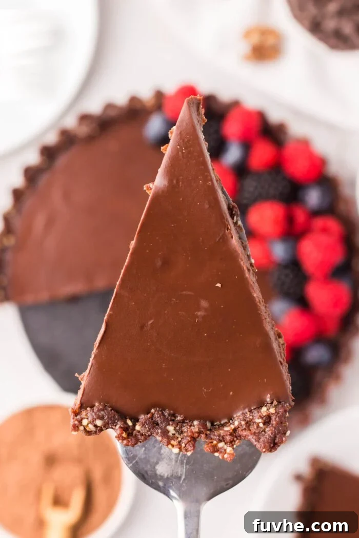 A slice of dark chocolate ganache tart on a spatula held over the whole tart underneath it.