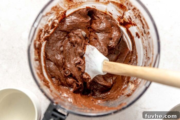 Decadent Vegan Avocado Brownies 6 Chocolate brownie batter in a food processor container with a spatula resting in it.