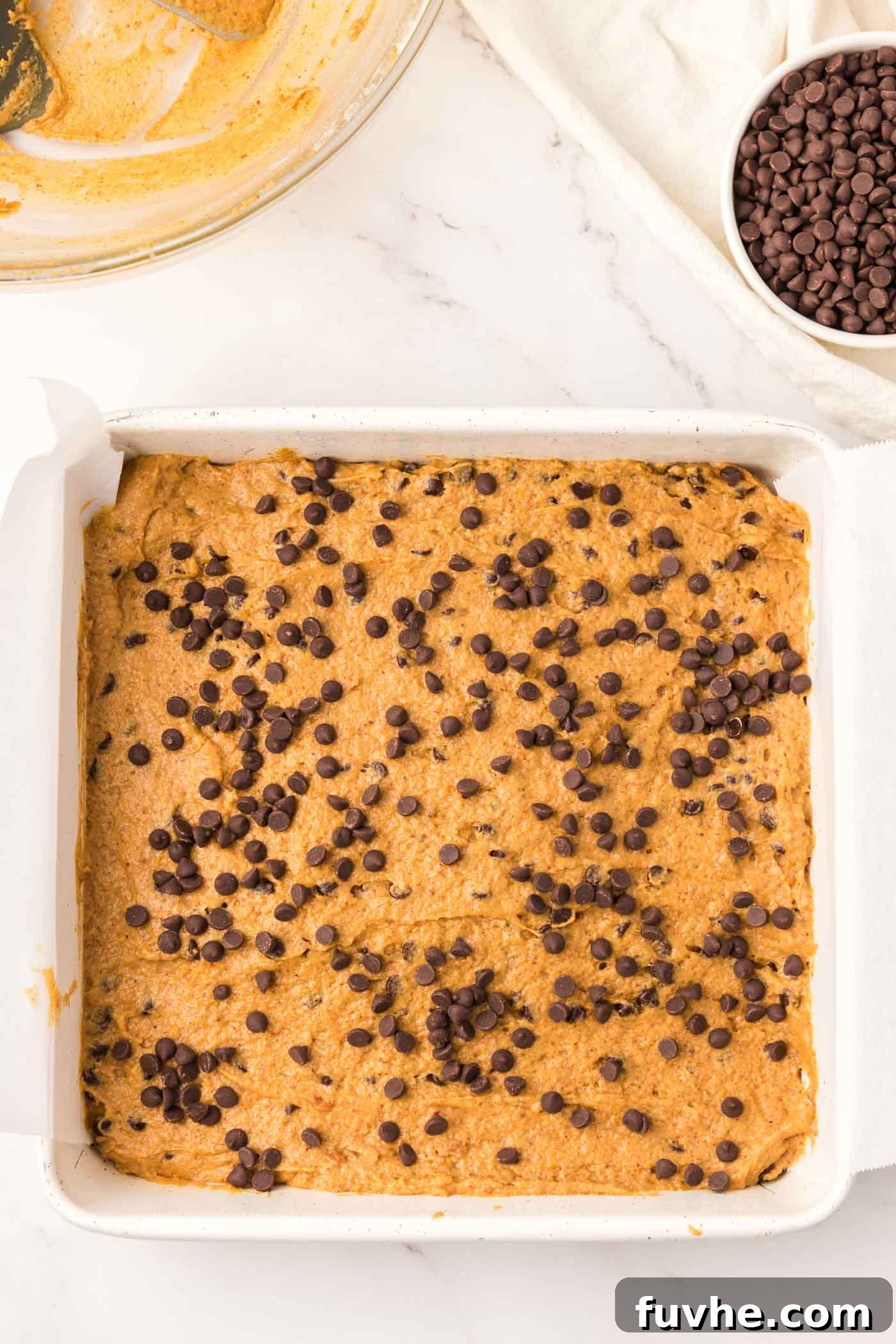 Spiced Vegan Pumpkin Chocolate Chip Bars 5 Unbaked pumpkin chocolate chip bar batter spread evenly in a baking pan lined with parchment paper.