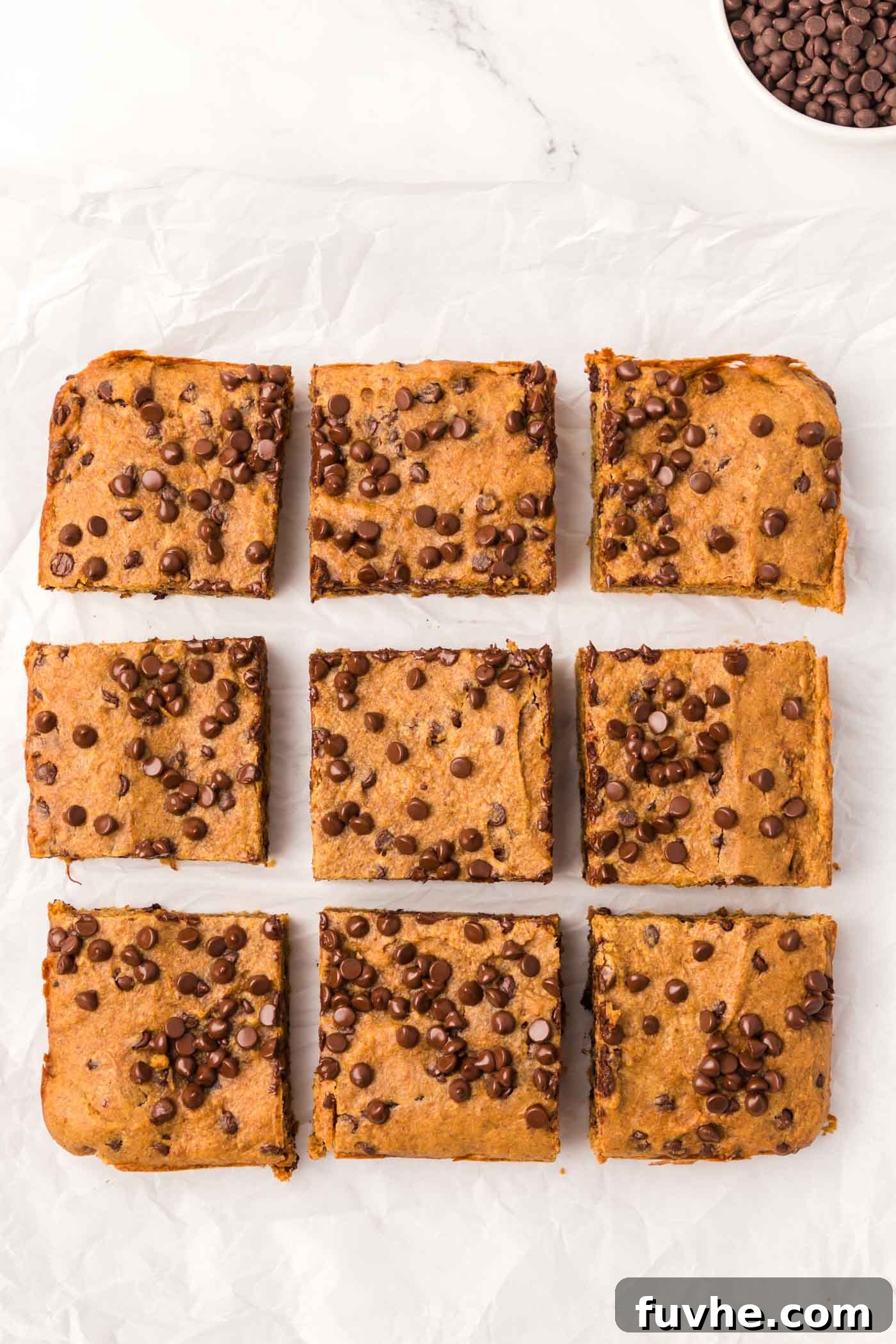 Spiced Vegan Pumpkin Chocolate Chip Bars 6 Baked vegan pumpkin chocolate chip bars cut into 9 squares on a piece of parchment.