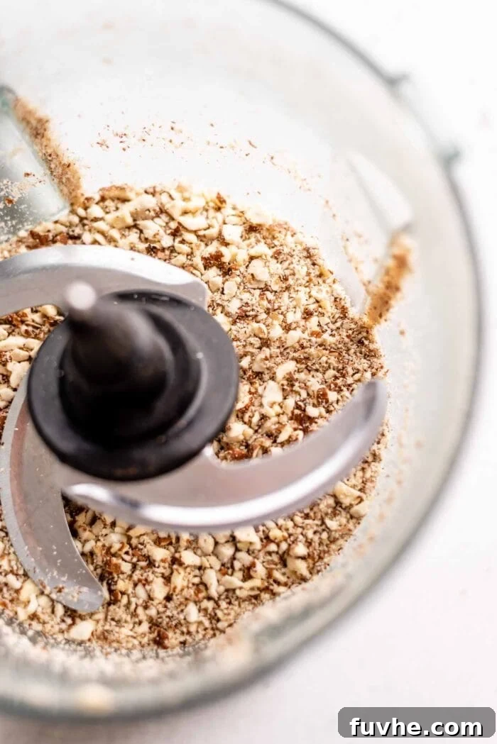 Blended almonds in a food processor, appearing as a coarse, grainy flour with some small chunks.