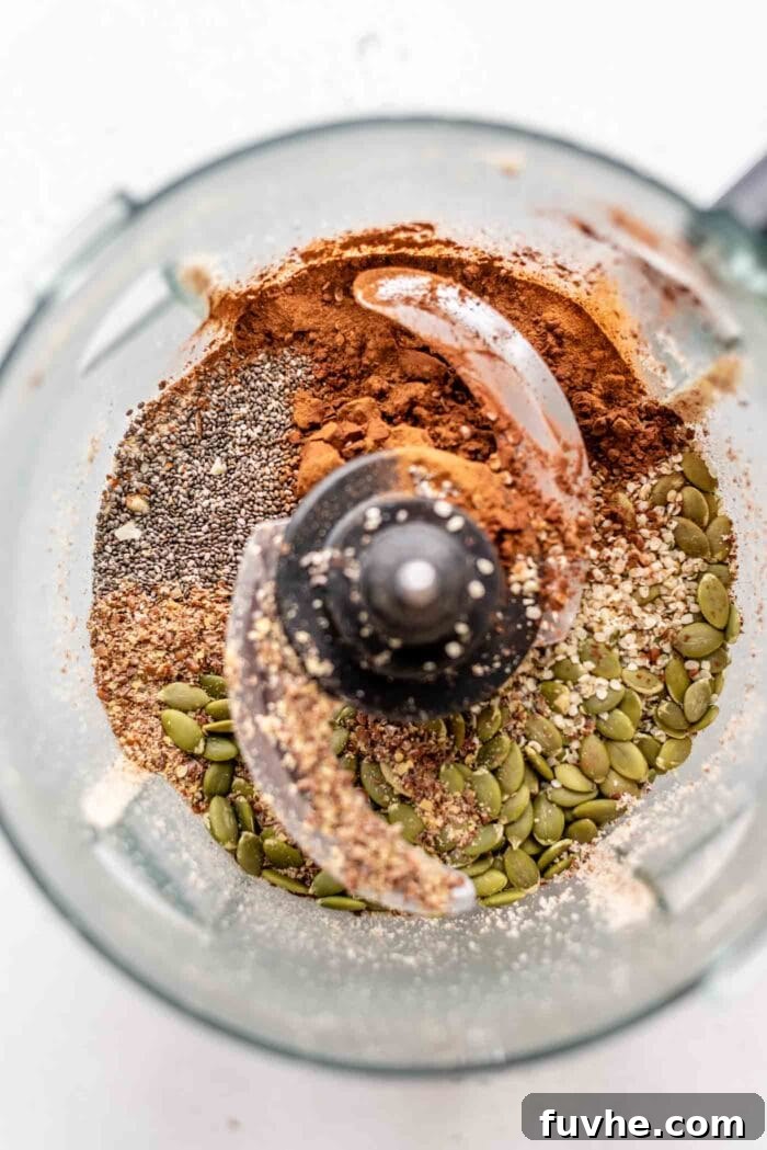 A mix of chia seeds, pumpkin seeds, cocoa powder, and hemp seeds added to the blended almonds in a food processor.